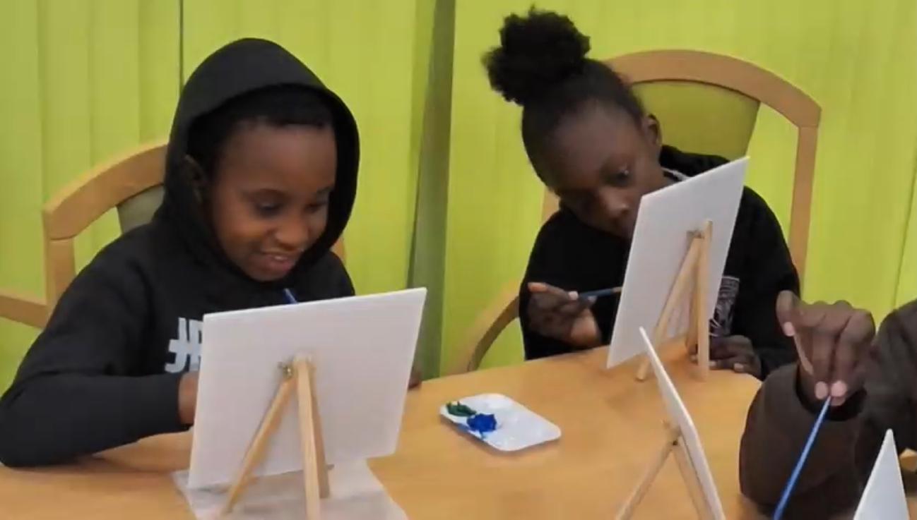 Children smiling while painting on small easels